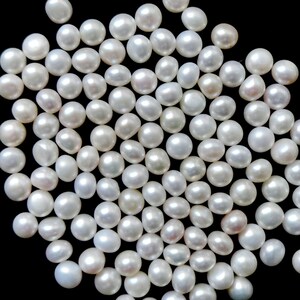 May include: A large group of white, round pearls scattered on a black background. The pearls are smooth and glossy, and they are all about the same size.