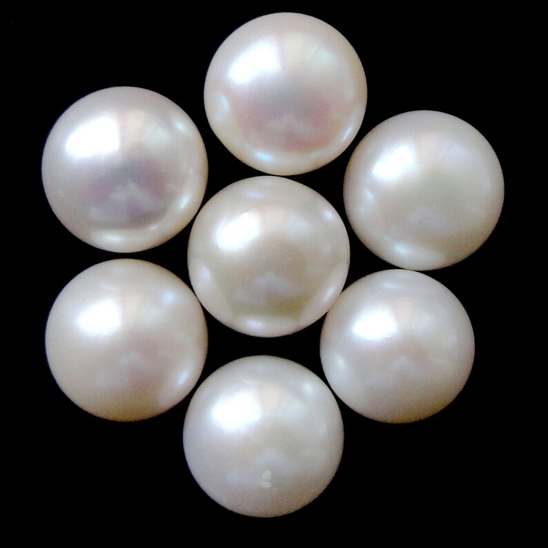 May include: Seven white round pearls arranged in a flower shape on a black background.