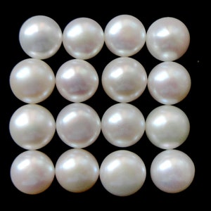 May include: A collection of 16 white round pearls arranged in a grid pattern.