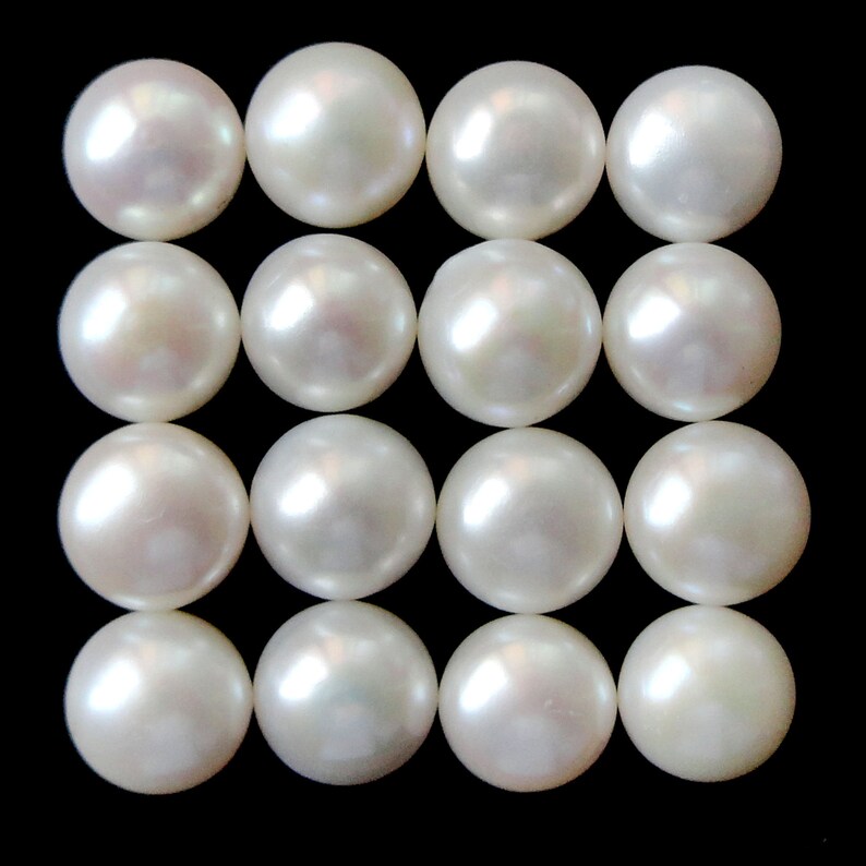 May include: A collection of 16 white round pearls arranged in a grid pattern on a black background.