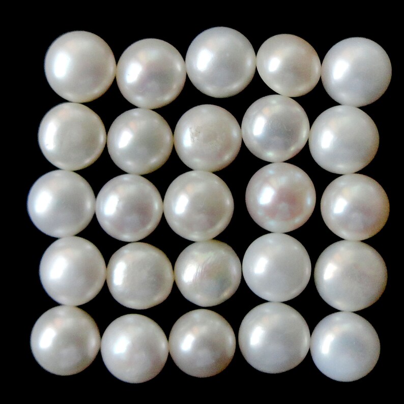 May include: A collection of 25 white round pearls arranged in a grid pattern on a black background.