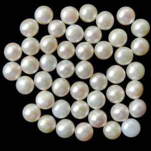 May include: A collection of white round pearls, scattered on a black background.