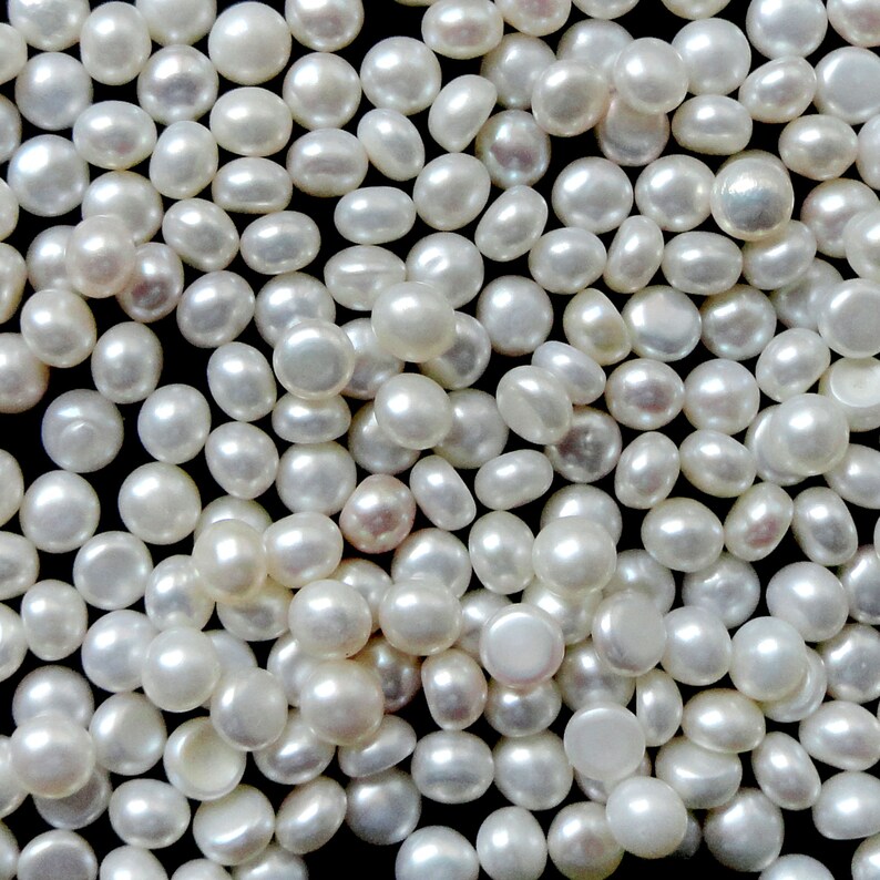 May include: A close-up image of a large quantity of white, round pearls. The pearls are scattered on a black surface.