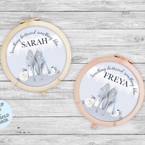 May include: Two round, compact mirrors with a gold and rose gold finish. The mirrors feature a blue background with white lace and silver high heels. The text "Something borrowed, something blue" is written around the edge of the mirrors. The names "Sarah" and "Freya" are written in the center of the mirrors. A separate image shows a choice of gold or rose gold mirror.