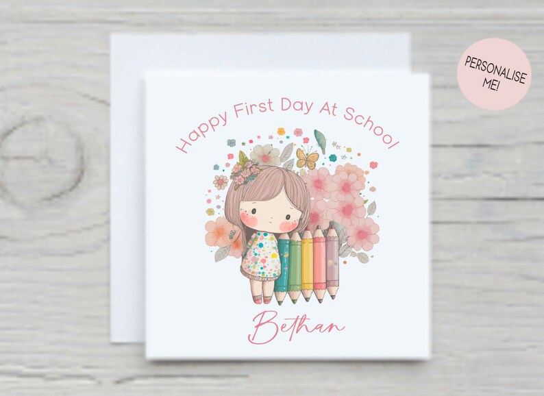 Puede incluir: Una tarjeta blanca con una ilustraci&oacute;n rosa y blanca de una ni&ntilde;a sosteniendo l&aacute;pices de colores. El texto "Happy First Day At School!" est&aacute; escrito en rosa encima de la ni&ntilde;a. El nombre de la ni&ntilde;a "Bethany" est&aacute; escrito en rosa debajo de la ni&ntilde;a.