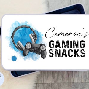 May include: White metal lunchbox with a blue watercolor design of a video game controller and headphones. The text "Cameron's Gaming Snacks" is printed in black.