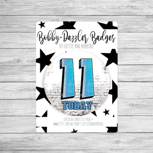 May include: A white and blue 11th birthday badge with black stars and the text "Bobby-Dazzler Badges" and "TODAY".