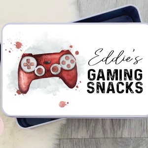 May include: A white tin with a red watercolor illustration of a video game controller. The text "Eddie's Gaming Snacks" is printed in black on the tin.