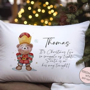 May include: White pillow with a watercolor illustration of a teddy bear wearing a crown and a festive outfit. The pillow has the name "Thomas" and the text "It's Christmas Eve so snuggle up tight. Santa is on his way tonight!"