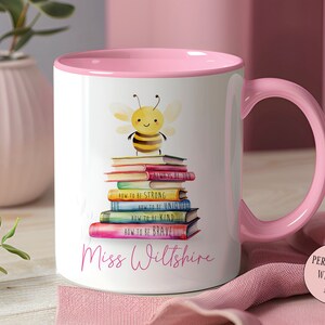 May include: A white ceramic mug with a pink rim and handle. The mug features a cartoon bee sitting on a stack of colorful books with the text "How to be strong", "How to be unique", "How to be kind", "How to be brave" and "Always be true" on the books. The mug is personalized with the name "Miss Wiltshire".