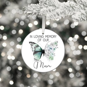 May include: White round Christmas ornament with a green and black butterfly and white flowers. The ornament reads "In loving memory of our Mum".