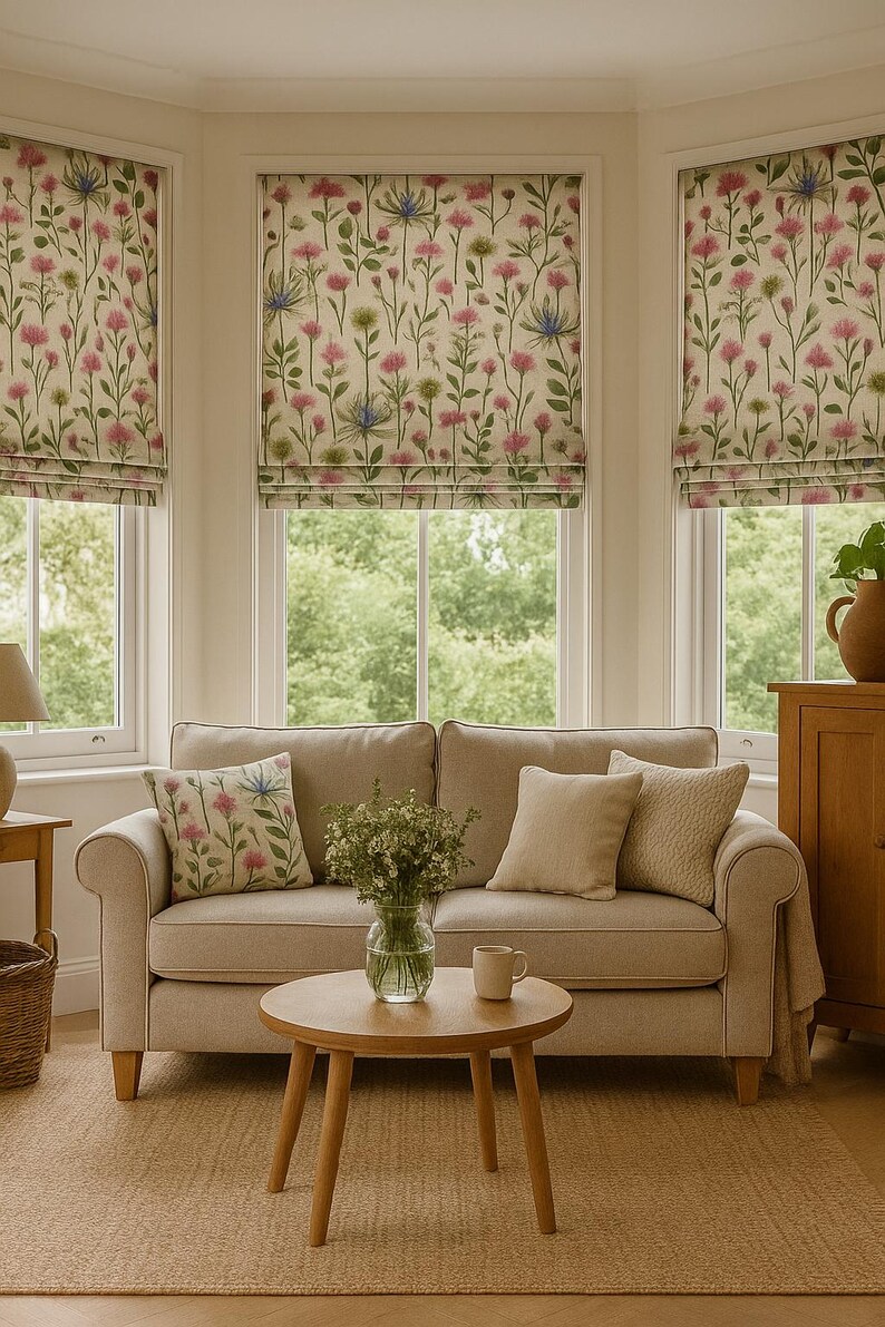 Bay window living room with wildflower Roman blinds in floral linen-look fabric, styled with beige sofa and botanical cushions