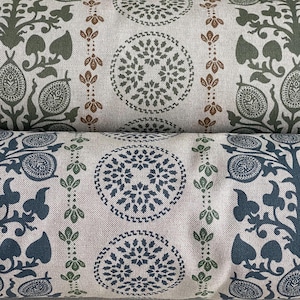 May include: Close-up of two fabric rolls with repeating patterns. The top roll features olive green and brown floral and circular designs on a beige background. The bottom roll has navy blue and green patterns on a similar beige fabric. The patterns include stylized leaves and circular motifs.