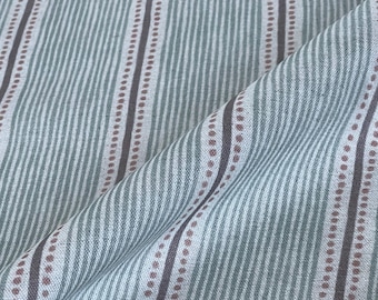 Op de afbeelding: Close-up van een stof met een streepjespatroon. De stof heeft verticale strepen in tinten blauwgroen, wit en bruin. Sommige strepen zijn effen, andere hebben een stippenpatroon. De stof is gevouwen en toont zijn textuur.