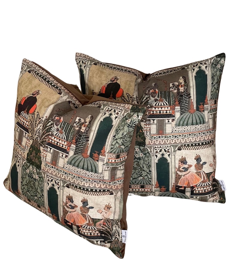 Puede incluir: Dos almohadas decorativas con fondo marr&oacute;n y estampado colorido de inspiraci&oacute;n india con personas, edificios y plantas.