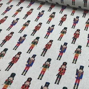 Puede incluir: Tela blanca con un patrón repetido de cascanueces de soldados de juguete rojo y azul. Los cascanueces sostienen un tambor y una espada.