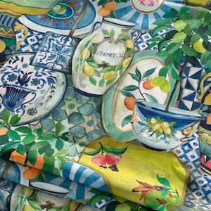 May include: A colorful fabric with a repeating pattern of blue and white ceramic dishes, green leafy plants, and lemons. The fabric features the text "Limoncello" on a large ceramic jar.