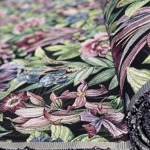 May include: Close-up of a black fabric with a floral tapestry design. The fabric features a variety of flowers in shades of pink, purple, and blue, as well as green leaves. The fabric is woven with a textured pattern.