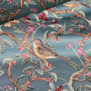 May include: Teal fabric with a detailed pattern of birds perched on branches with red and pink flowers. The birds have brown and tan feathers, and the branches are a warm brown color. The fabric has a woven texture.