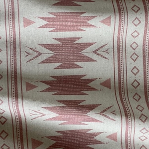May include: Close-up of a fabric with a repeating geometric pattern in dusty rose and off-white. The design features stylized arrowheads and diamond shapes, creating a Southwestern or tribal aesthetic. The fabric has a textured appearance.
