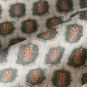 Könnte beinhalten: Nahaufnahme eines gemusterten Stoffes mit sich wiederholendem Design. Das Muster umfasst olivgrüne, beige und rostfarbene blattartige Formen in einem geometrischen Rahmen. Der Stoff hat ein strukturiertes Aussehen, möglicherweise Leinen oder ein ähnliches Gewebe.