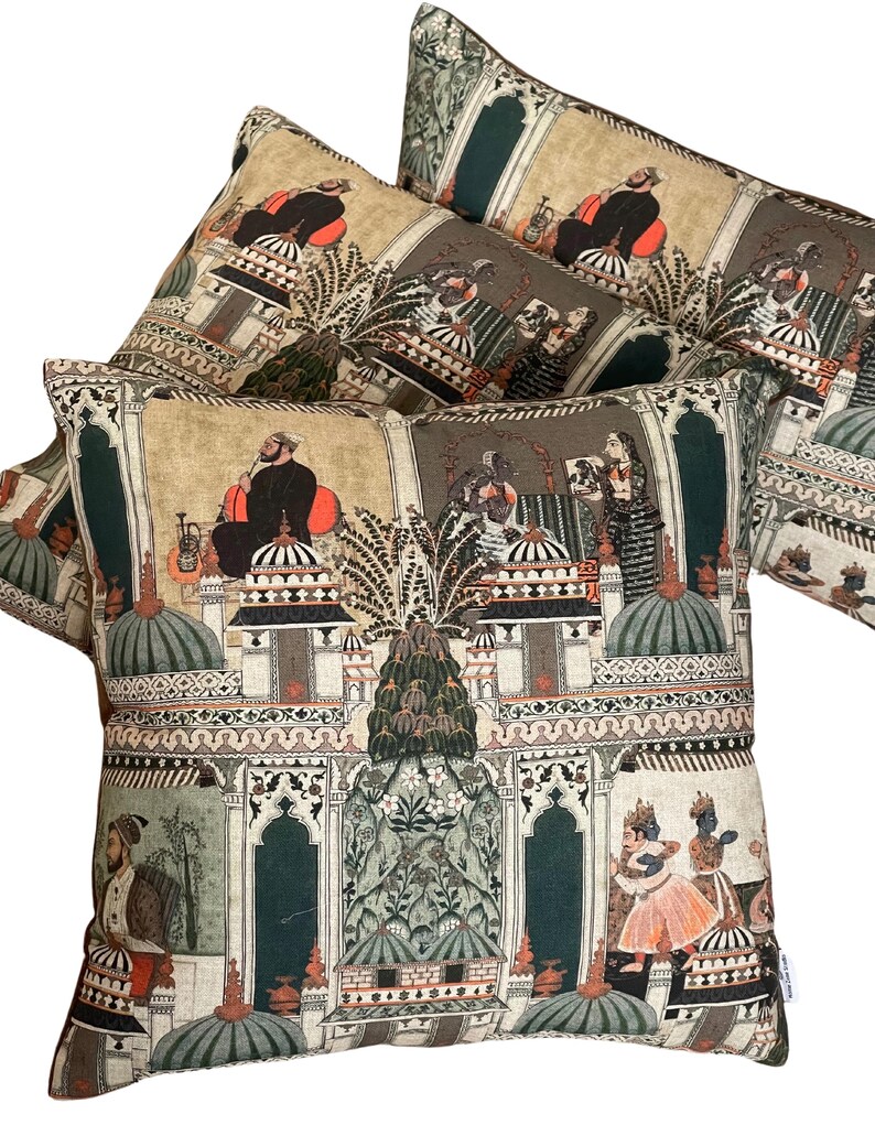 Puede incluir: Tres almohadas decorativas con un fondo beige y un patr&oacute;n repetido de ilustraciones verdes, naranjas y negras de personas y edificios. Las ilustraciones recuerdan al arte tradicional indio.