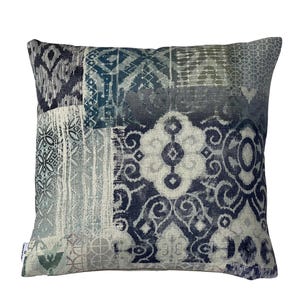 May include: Square decorative pillow with a patchwork design in shades of blue, gray, and cream. The pillow features various geometric and abstract patterns, creating a textured and visually interesting surface. The overall aesthetic is a blend of modern and bohemian styles.