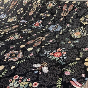 May include: Black fabric with a repeating pattern of colorful flowers, butterflies, and jewelry. The fabric has a textured, woven look.