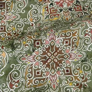 May include: A green fabric with a white, brown, and pink paisley pattern. The fabric has a textured surface and a slightly faded look.