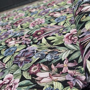 May include: Black fabric with a floral pattern featuring pink, purple, and blue flowers on a dark green background. The fabric is woven with a textured, raised design.