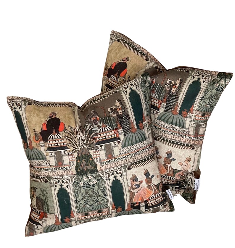 Puede incluir: Dos almohadas decorativas con fondo beige y un estampado colorido de inspiraci&oacute;n india con personas, edificios y plantas. El estampado es en tonos rojos, naranjas, verdes, azules y negros.