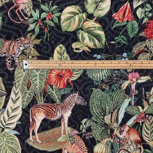 Op de afbeelding: Een zwarte tapijtstof met een jungle thema. De stof heeft een zebra, een jaguar, apen en verschillende tropische planten en bloemen. De stof is geweven met een textuur, verhoogd ontwerp.