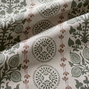 Könnte beinhalten: Nahaufnahme eines Stoffes mit sich wiederholendem Muster. Das Design zeigt olivgrüne und braune Blumen- und Kreis-Motive auf beigem Hintergrund. Der Stoff hat ein strukturiertes Aussehen und ist gefaltet.