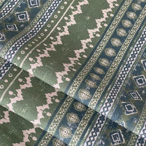 May include: Close-up of folded fabric with a repeating pattern. The design features vertical stripes in shades of green, white, and navy blue. The fabric has a textured appearance, with geometric and floral motifs.