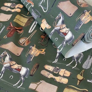 May include: Green fabric with a repeating pattern of horses, saddles, and other equestrian equipment. The fabric is folded over, showing the white backing.