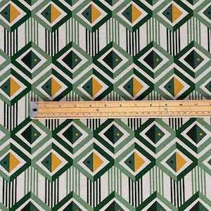 Peut inclure: Tissu à motifs géométriques avec des losanges répétés verts, jaunes et vert foncé. Des rayures verticales et une règle en bois avec des mesures en centimètres sont visibles. Le tissu a un aspect texturé.