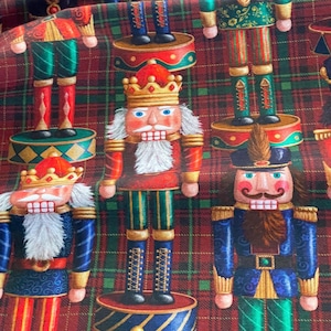 Puede incluir: Una tela de cuadros rojos, verdes y azules con un patrón repetido de figuras de cascanueces. Los cascanueces llevan uniformes coloridos y tienen caras pintadas.
