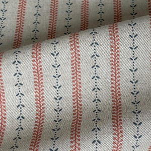 Peut inclure: Gros plan sur un tissu à motif répétitif. Le tissu présente des rayures verticales de couleur beige clair. Des rayures alternées présentent un motif rouge en forme de feuille et une série de petites formes bleues en forme de flèche.