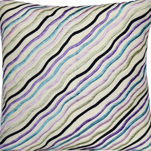 Puede incluir: Cojín cuadrado con fondo crema y rayas onduladas diagonales en tonos azules, morados, verdes y negros. Las rayas tienen un aspecto texturizado y en relieve. Este cojín decorativo es ideal para la decoración del hogar.