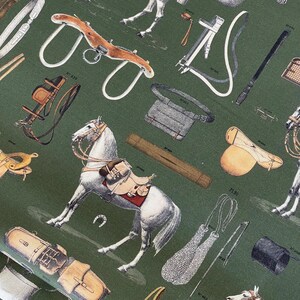 May include: A green fabric with a white horse and various equestrian equipment, including saddles, bridles, stirrups, and a whip. The fabric has a vintage feel and is perfect for a horse-themed project.
