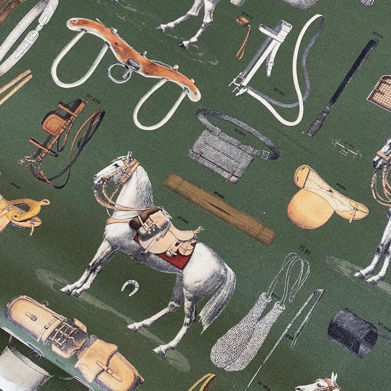 May include: A green fabric with a white horse and various equestrian equipment, including saddles, bridles, stirrups, and a whip. The fabric has a vintage feel and is perfect for a horse-themed project.