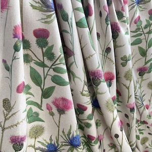 Natural linen-look fabric with wild thistle floral design, featuring folded texture and delicate country garden hues – ideal for soft furnishings.