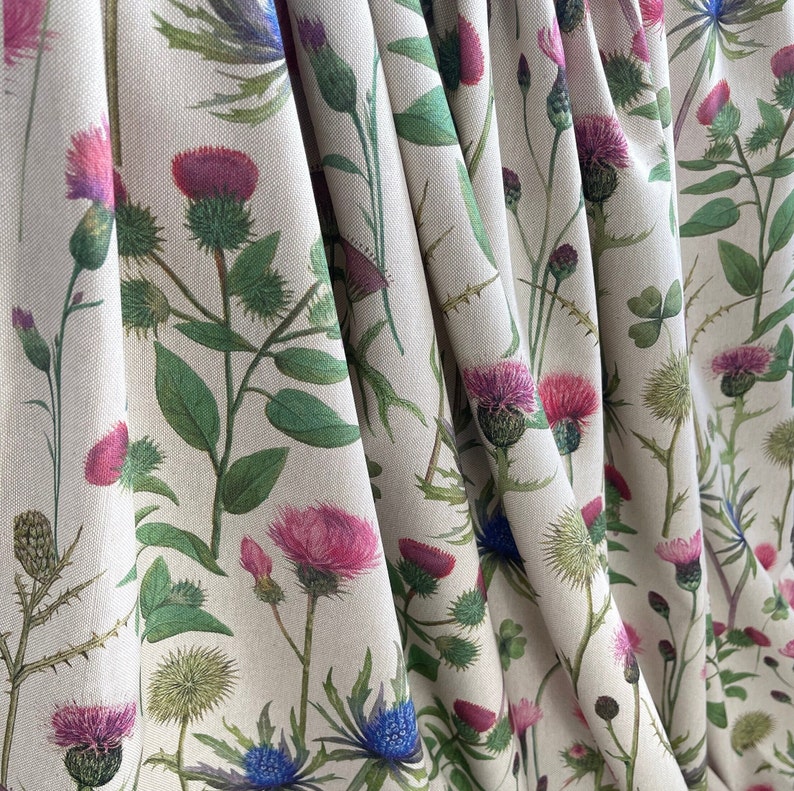Natural linen-look fabric with wild thistle floral design, featuring folded texture and delicate country garden hues – ideal for soft furnishings.