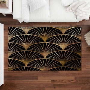 May include: Black and gold art deco style area rug. The rug features a repeating fan pattern in gold against a black background. The rug is rectangular and appears to be made of a soft material. The rug is placed on a hardwood floor.