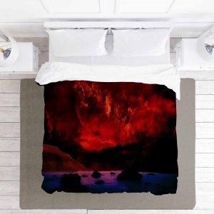 May include: A red and black duvet cover with a large red planet and clouds in the background. The planet is surrounded by a dark blue body of water with rocks and a shoreline.