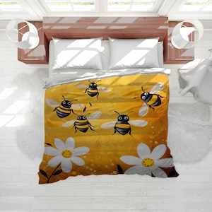 Puede incluir: Una funda nórdica amarilla y naranja con abejas de dibujos animados y margaritas blancas. Las abejas tienen cuerpos a rayas negras y amarillas y alas blancas. La funda está sobre una cama con almohadas blancas y un cabecero de madera.