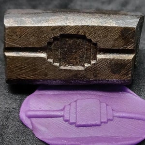 May include: A close-up of a metal stamp with a geometric design. The stamp is used to create a purple wax seal with the same design. A ruler is included for scale, showing the seal is approximately 1 1/2 inches wide.