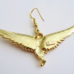 K&ouml;nnte beinhalten: Goldfarbene Ohrringe in Vogelform mit einem detaillierten Design. Die Ohrringe sind mit den Buchstaben "O.J.J." gekennzeichnet.