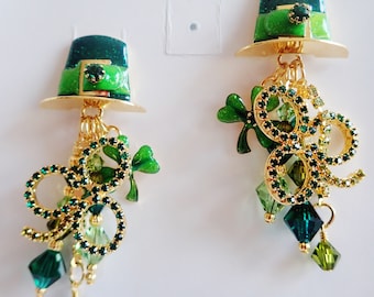 May include: A pair of gold dangle earrings with green shamrock charms and green and gold hats. The hats have a green glitter finish.