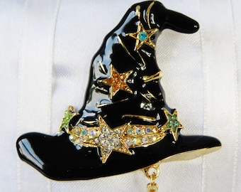 May include: A black witch's hat with gold trim and a dangling star charm. The hat is decorated with rhinestones and colorful stars.